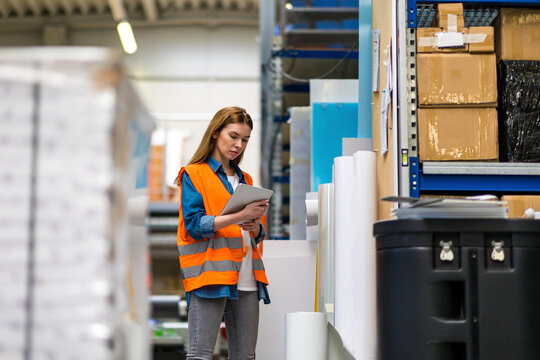 Woman with tablet in factory storehouse checking location of goods