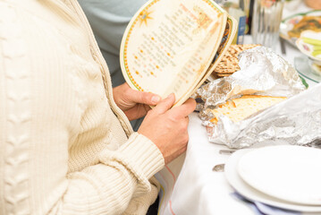 Jewish family celebrates Passover Seder. Mans hands holding Haggadah. Young man reads the Passover Haggadah. Matzo for afikoman on the table.Selective focus.