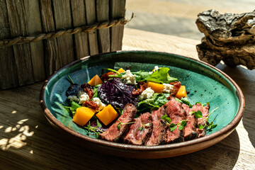 Baked pumpkin salad, spinach, tomato and beef in a white plate on a stone background, top view