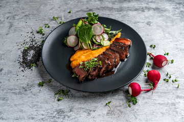 A deliciously appetizing pumpkin puree with chunks of beef meat with spices and herbs in a green plate on a dark stone table. A hearty lunch in a restaurant. Meat with vegetables in the oven