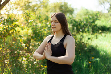 A girl meditates during a yoga class in a summer park. Sunny weather, taking care of the soul and body