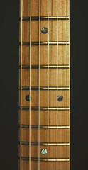 The neck of a six-string classical electric guitar on a gray background. Isolated neck without lining with electric guitar dots on a dark background. Wooden neck of an electric guitar.