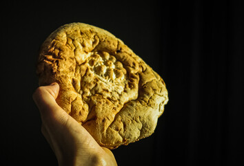 A fresh flatbread in a man's hand in close-up on a dark background with selective focus. A flatbread in a man's hand close-up. Traditional bread.