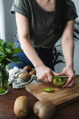 Woman in the kitchen slicing kiwis. Girl preparing fresh and juicy fruit
