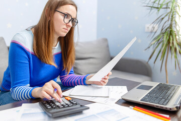 Woman using calculator for calculate domestic bills at home, doing paperwork for paying taxes
