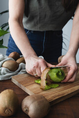 Woman in the kitchen slicing kiwis. Girl preparing fresh and juicy fruit