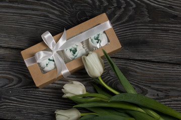 Roses, tulips and chrysanthemums from marshmallows. Zephyr flowers. In craft packaging. Tied with ribbon. Nearby is a bouquet of white tulips.