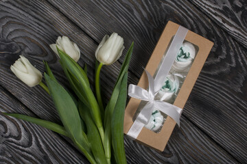 Roses, tulips and chrysanthemums from marshmallows. Zephyr flowers. In craft packaging. Tied with ribbon. Nearby is a bouquet of white tulips.