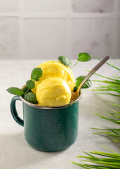 Balls of homemade yellow fruit ice cream with fresh mint in a metal mug on a light background....