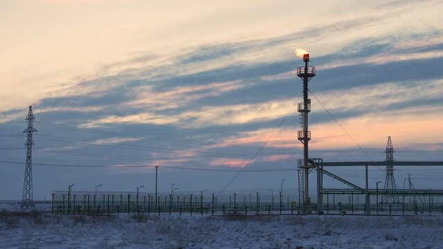 Burning GAS FLARE rises from REFINERY stack against a winter SKY in remote INDUSTRIAL zone.