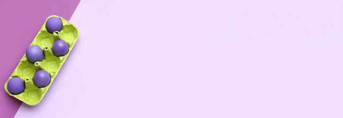 Holder with painted Easter eggs on lilac background with space for text