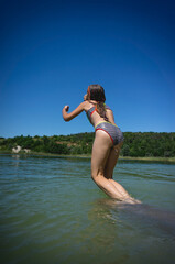 Naklejka premium A little cute girl in a swimsuit jumps into the blue water of a career lake.