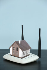 Modern wi-fi router and figure of house on table against light blue background