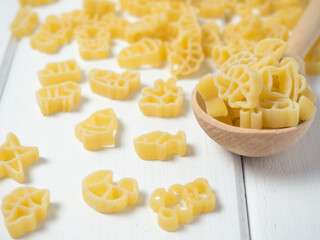 raw children's pasta in the form of different animals, stars and bells on a wooden spoon
