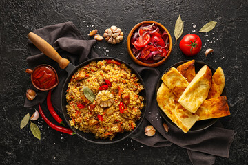 Frying pan of tasty Asian pilaf and flatbread with vegetable salad on dark background
