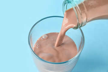 Pouring of delicious chocolate milk from bottle into glass on color background