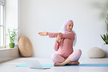Young pregnant Muslim woman practicing yoga with laptop at home