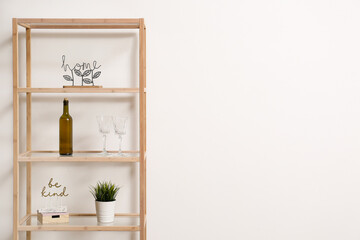Shelving unit with bottle of wine, glasses and decor near light wall