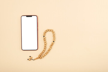 Top view of smartphone with white screen, next to a rosary on a beige background, mockup