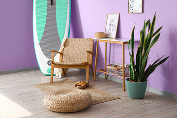 Comfortable armchair, pouf and board for sup surfing near color wall in room interior