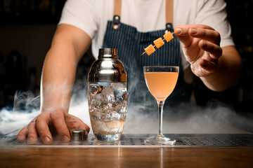 Glass of orange cold cocktail and transparent shaker with ice on the bar counter