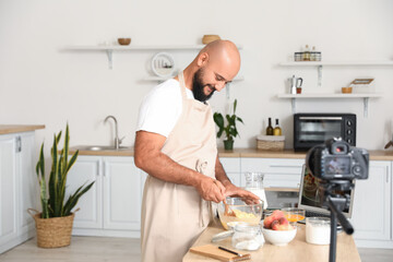 Handsome man making dough while recording video tutorial in kitchen