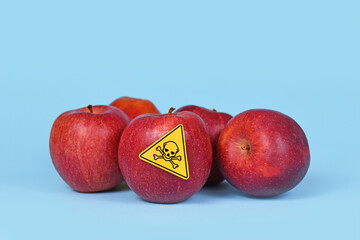 Red apples with poison skull symbol sticker on blue background. Concept of pesticide residues in agricultural food - obrazy, fototapety, plakaty