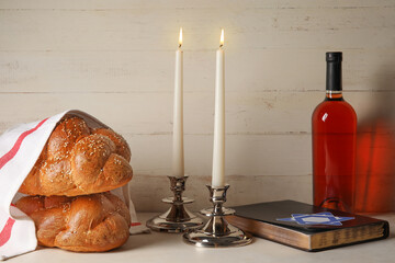 Traditional challah bread with glowing candles, Torah and bottle of wine on white wooden...