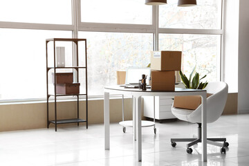 Cardboard boxes with belongings and furniture in interior of office on moving day