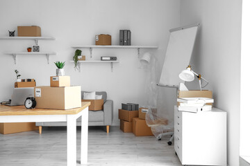 Cardboard boxes with belongings and furniture in interior of office on moving day