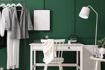 Comfortable workplace, rack and blank photo frame on green wall in room
