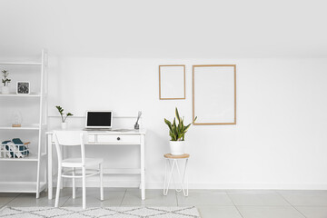 Interior of light room with modern workplace, shelving unit and frames