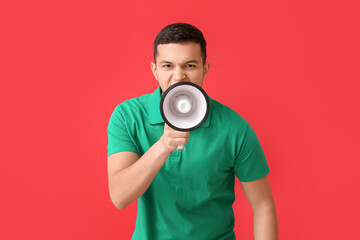 Angry young man shouting into megaphone on red background