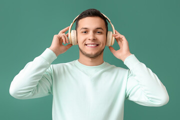 Fototapeta premium Young man in wireless headphones listening to music on green background