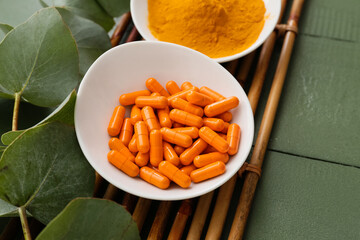 Plates with turmeric capsules and powder on color wooden background, closeup