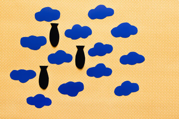 Top view of carton clouds and paper bombs on textured yellow background.