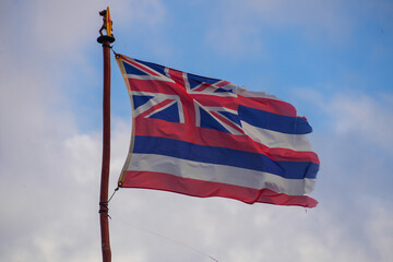 Hawaiian flag in the wind on a red pole in front of a blue sky