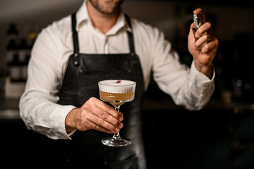 Professional bartender sprays on cold orange foamy alcoholic drink