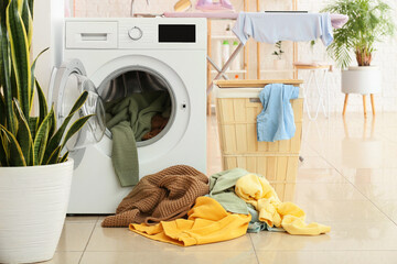 Modern washing machine with laundry, basket and plant in bathroom