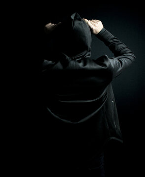 Man standing alone in the dark wearing a black hoodie and hat