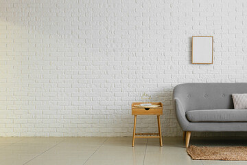 Comfortable sofa and table with stylish decor near white brick wall in room