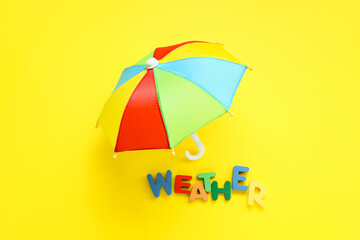 Mini umbrella and word WEATHER made of colorful letters on yellow background