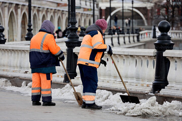 Snow removal in spring city, janitors with shovels. Two women workers cleaning a street