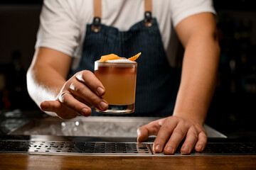 Fototapeta na wymiar barman's hand holds transparent glass with 3 layer cocktail decorated with orange zest