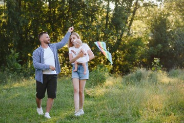 Obraz premium Young beautiful family with a little daughter hug, kiss and walk in nature at sunset. Photo of a family with a small child in nature.