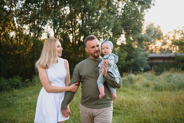 Young beautiful family with a little daughter hug, kiss and walk in nature at sunset. Photo of a family with a small child in nature.