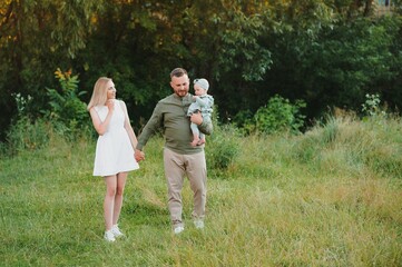 Young beautiful family with a little daughter hug, kiss and walk in nature at sunset. Photo of a family with a small child in nature.