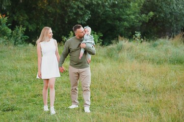 Obraz premium Young beautiful family with a little daughter hug, kiss and walk in nature at sunset. Photo of a family with a small child in nature.