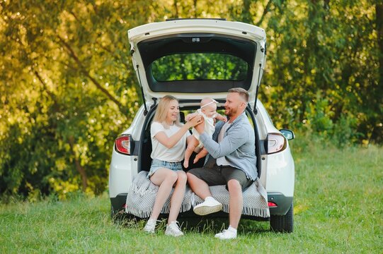 Young family three people in white clothes have picnic. Beautiful parents and daughter travel by car during summer vacation. Scene in park
