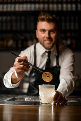 Bartender decorates cocktail glass with dried orange using tweesers.